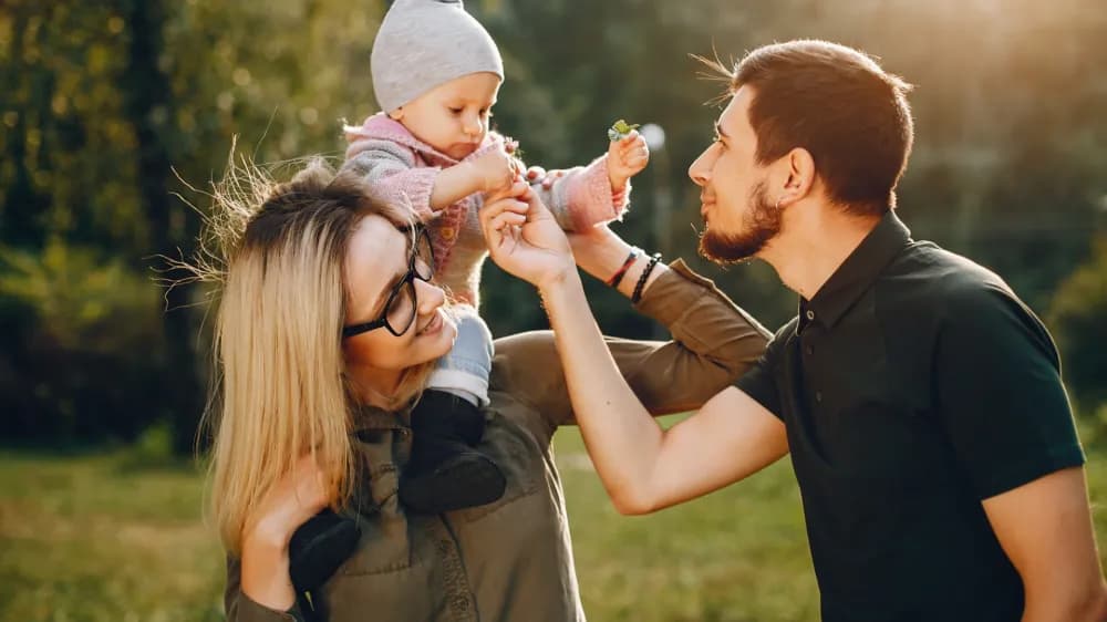 Family with a baby on their shoulders in a park during a family day