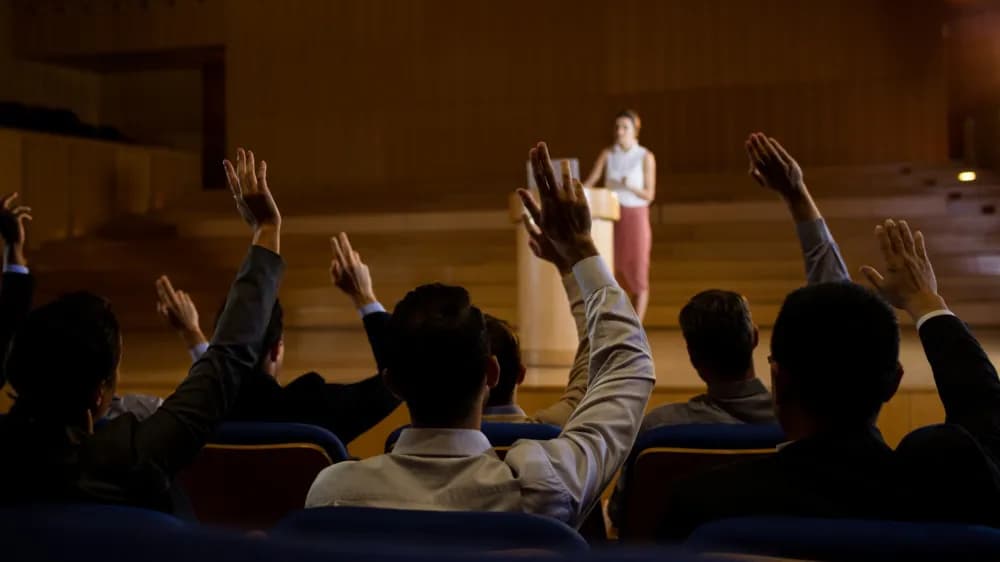 Profile cover: speaker on a stage in front of an audience with raised hands