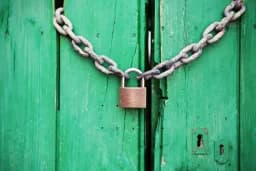 Cadena con candado cerrada sobre una puerta de madera verde